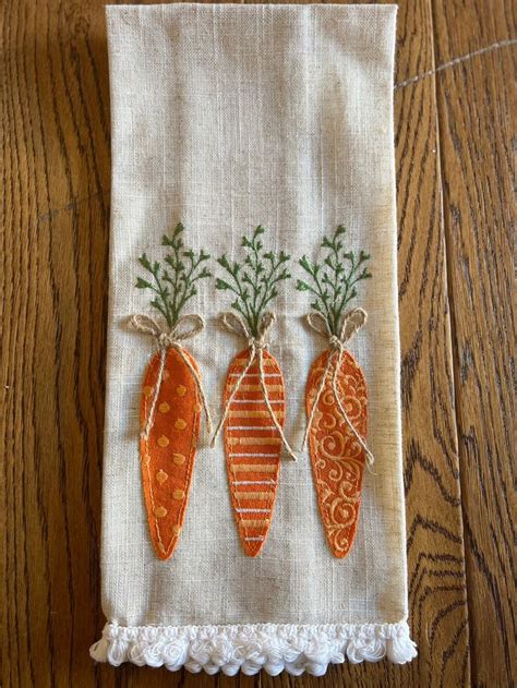 Three Embroidered Carrots On A White Linen Dish Towel Hanging From A