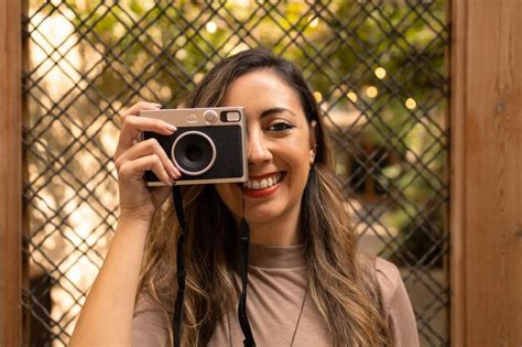 Joven turista latina adulta sonriendo y tomando una foto con una cámara vintage durante un viaje
