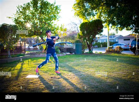 Young asian girl hitting baseball in front yard during sunset Stock