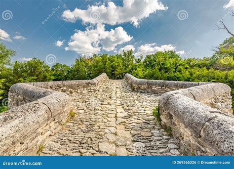 Rock Stone Bridge Across Small Pond With Green Trees Under Blue Sky