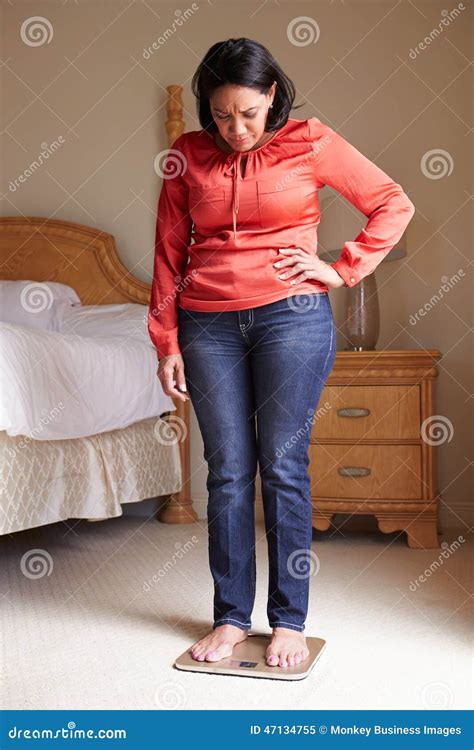 Overweight Woman Weighing Herself On Scales In Bedroom Stock Image