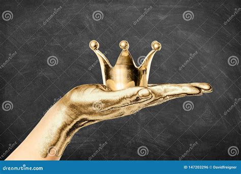 Gilded Female Hand Holding A Golden Crown With Dark Chalkboard