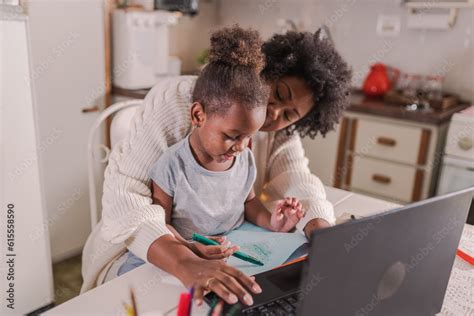 mulher Latina negra trabalhando em seu computador portátil na mesa da cozinha sua filha