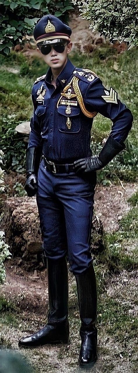 A Man In Uniform Standing Next To Some Bushes And Trees With His Hands