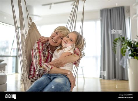 Caucasian Blonde Grandmother And Her Granddaughter Sitting In Hammock Hugging Smiling Stock