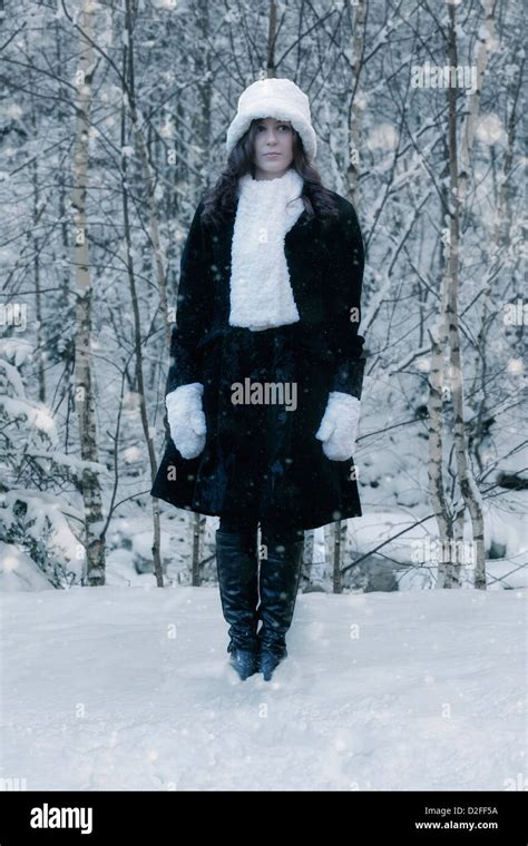 A Woman In A Black Coat With A White Hat And White Scarf In The Snow