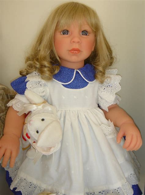 A Doll With Blonde Hair Wearing A White Dress And Holding A Stuffed