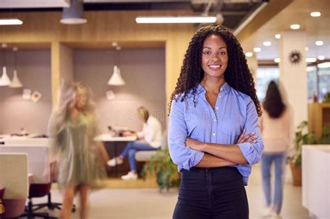 Portrait Of Businesswoman Standing In Busy Open Plan Office With Motion