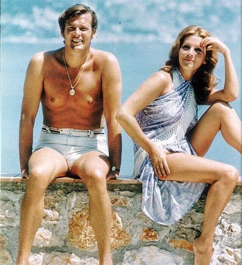 a man and woman sitting on a stone wall next to each other near the ocean