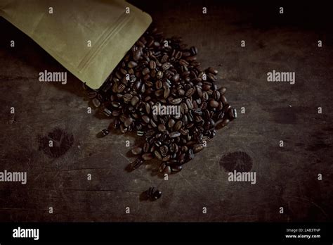 Coffee Beans Spill Out Of The Paper Pouch Bag On The Wooden Table Stock