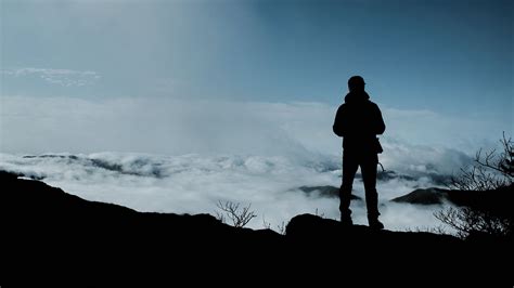 Sad Looking Man Is Standing Alone On Rock Edge In White Clouds Sky