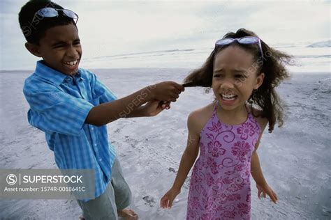 Boy pulling a girl's hair on the beach - SuperStock