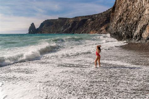 A Beautiful And Brunette In A Red Swimsuit On A Pebble Beach Running Along The Shore In The