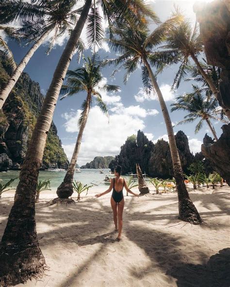 A Woman In A Bathing Suit Walking On The Beach With Palm Trees And