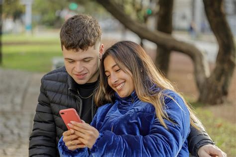 Chica latina apoyada en el hombro de su novio sentada en un banco en un parque público Foto