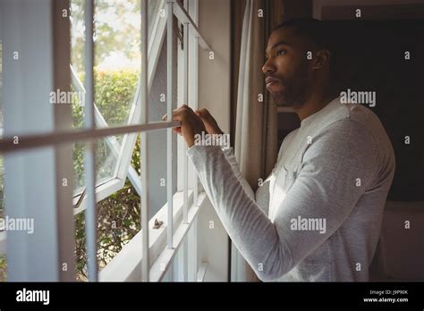 Side view of thoughtful man looking out through window while standing ...