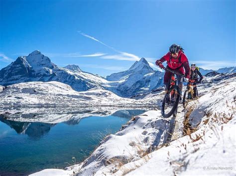 A Man Riding A Mountain Bike On Top Of A Snow Covered Slope Next To A Lake