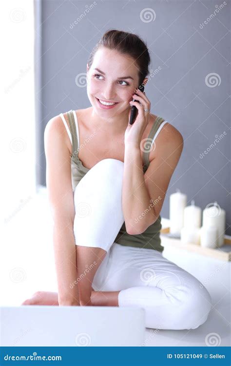 Smiling Beautiful Brunette Sitting On The Floor And Using Her Phone In The Living Room Stock
