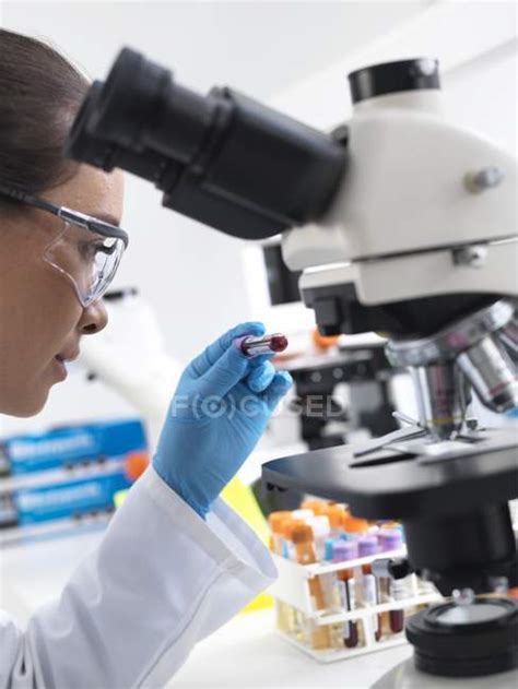 Female Scientist Holding Blood Sample By Microscope In Laboratory