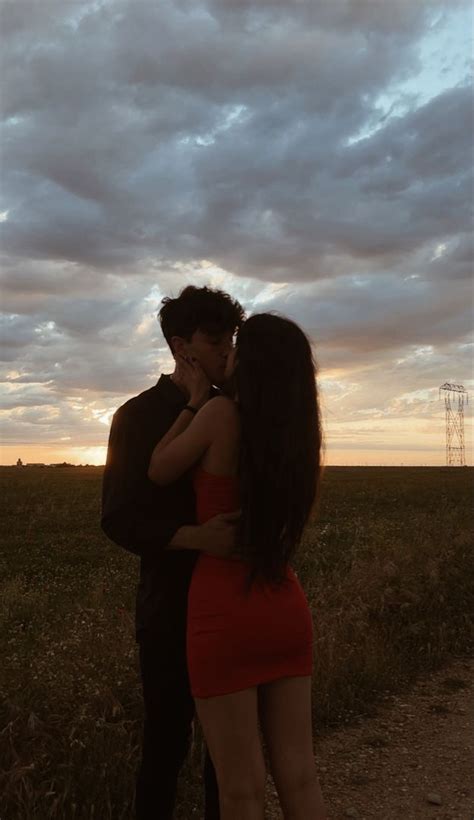 A Man And Woman Kissing In The Middle Of A Field At Sunset With Clouds