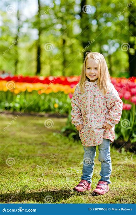 El Blonde Hermoso Muy Lindo De La Muchacha En Capa Rosada Se Coloca Cerca De Un Flowe Imagen De