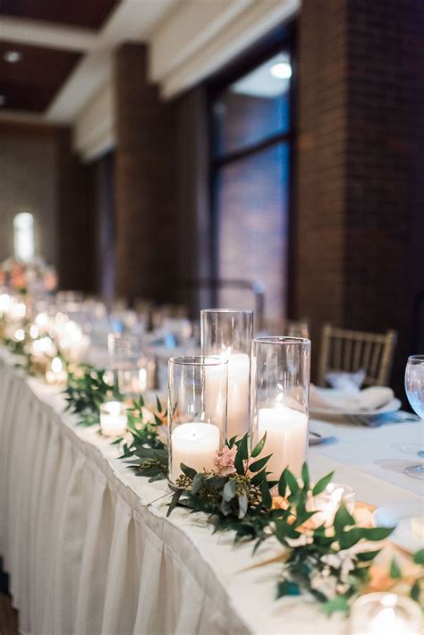 Head table decorated with green ruscus with a collection of cylinder ...