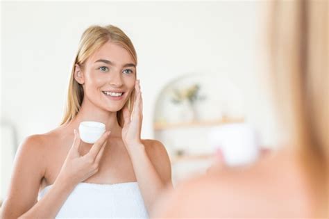 Premium Photo Blonde Woman Enjoys Applying Moisturizer To Face Skin In Bathroom