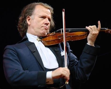 A Man In A Tuxedo Holding A Violin On Stage With One Hand And Looking