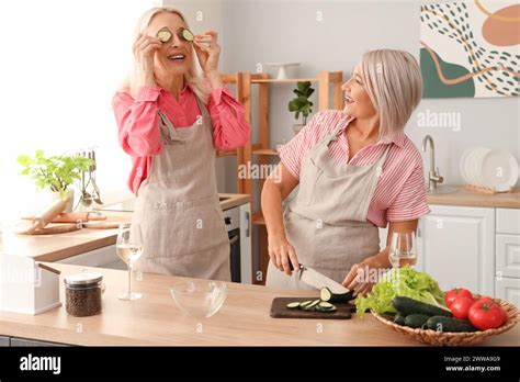 Mature Female Friends Cutting Cucumber In Kitchen Stock Photo Alamy