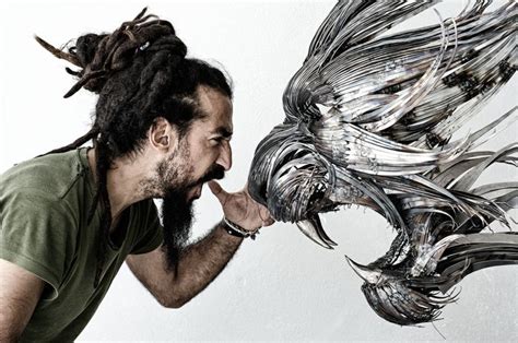 A Man With Dreadlocks Biting Into A Metal Sculpture