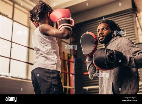 Boxing coach wearing punching pads in hands training a little girl ...