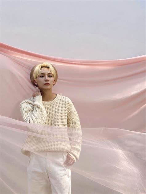 A Woman Standing In Front Of A Pink Backdrop Wearing White Pants And A