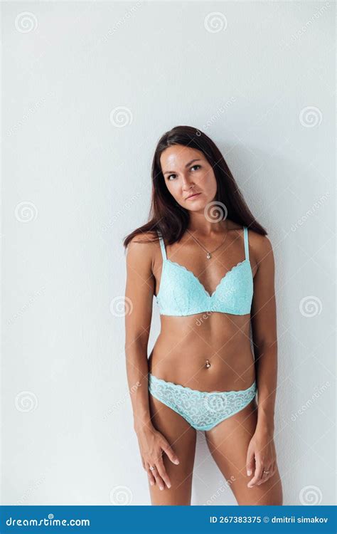 A Brunette Woman In Blue Lingerie Stands On A White Background Stock