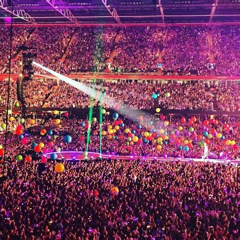 A Large Group Of People At A Concert With Balloons In The Air And Lights On