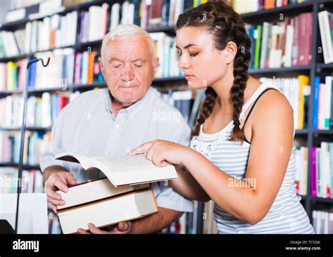 Old Man With Young Granddaughter Are Reading Books In Bookstore Stock