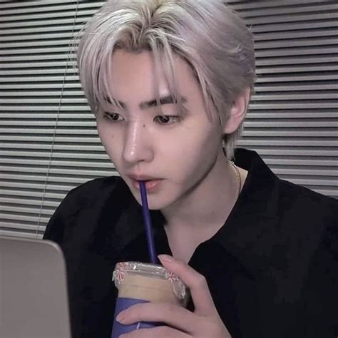 A Man With Blonde Hair Drinking From A Cup And Using A Laptop Computer While Holding A Straw In