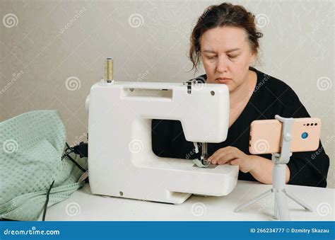 A Female Seamstress Sews Green Fabric Items On A Sewing Machine Stock