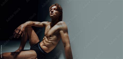 Hot Male Model Sit Nude And Erotic On Floor In Dark Blue Studio Look Up And Express His