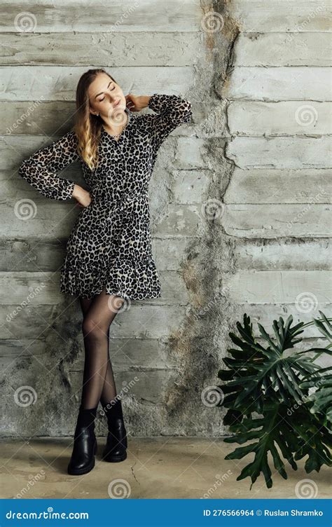 Beautiful Blonde Girl In A Gray Dress And Black Shoes Posing Against