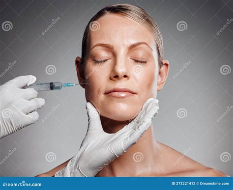 Beautiful Mature Woman Getting Botox Injection In Studio Against A Grey Background Stock Photo