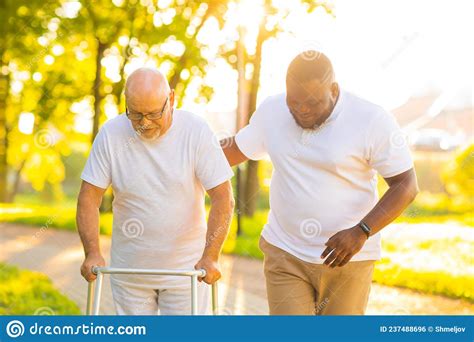 Caregiver Is Teaching Old Man To Walk With Walker Professional Nurse