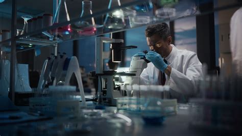 Female Scientist Looks At Biological Samples Under Microscope Side