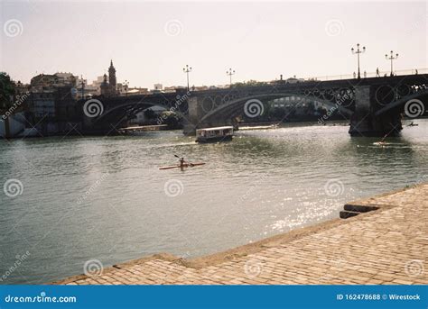 Concrete Bridge With Arches Over A Lake And People On Boats On A Sunny