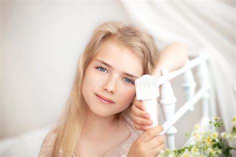Belle Petite Fille Blonde Aux Cheveux Longs Assise Sur Un Lit Avec Un Bouquet De Marguerites