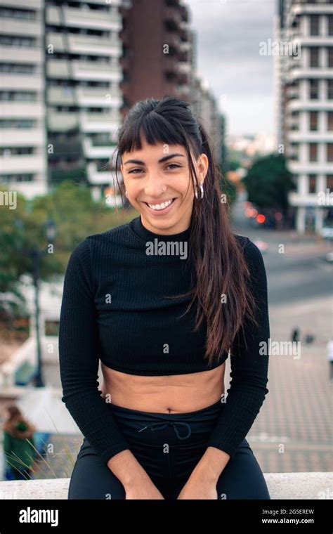 A Vertical Shot Of A Beautiful Argentine Brunette Girl Sitting On A Stone Surface In The City