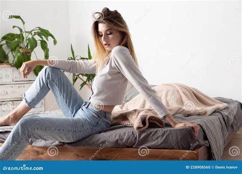 Glamorous Beautiful Model Girl With Blonde Hair In A Blouse And Jeans Is Sitting Posing On The