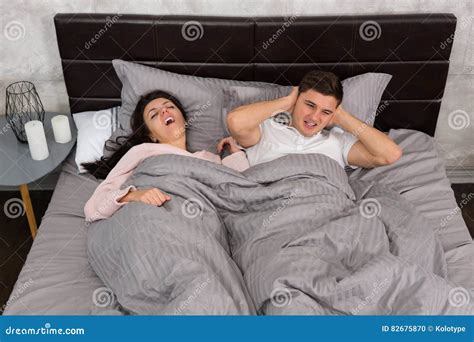 Young Man Can Not Sleep And Covers His Ears Because His Girlfriend Snoring While Sleeping Stock