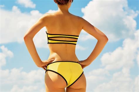 Detrás de la joven hermosa mujer con cuerpo perfecto de pie en la playa en bikini Foto Premium