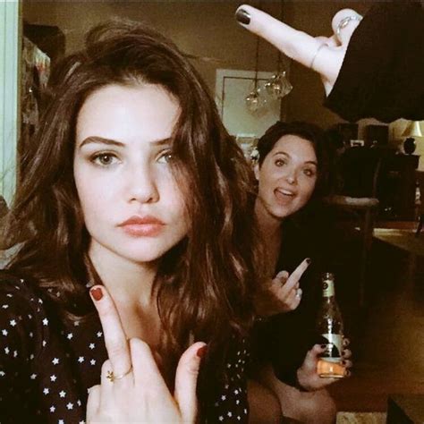 Two Women Sitting At A Table With One Pointing To The Camera And The Other Holding Her Finger Up