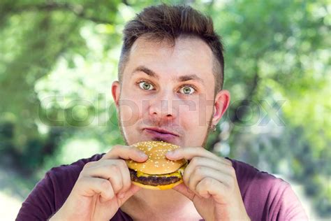 Emotional Young Guy Eating A Cheeseburger On The Nature Stock Image